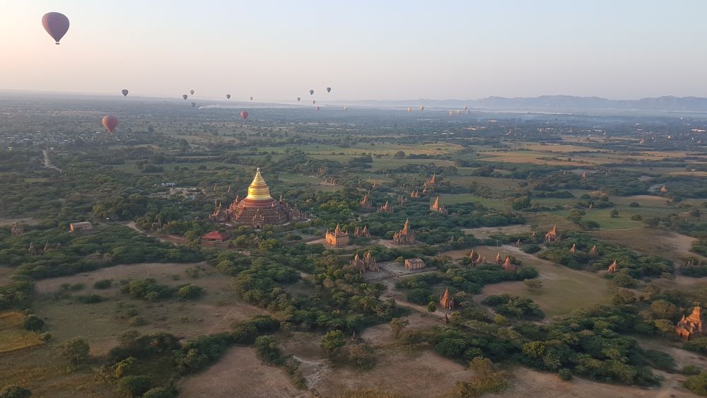 Luftaufnahme in Myanmar mit Tempeln und Heißluftballons bei Sonnenaufgang.